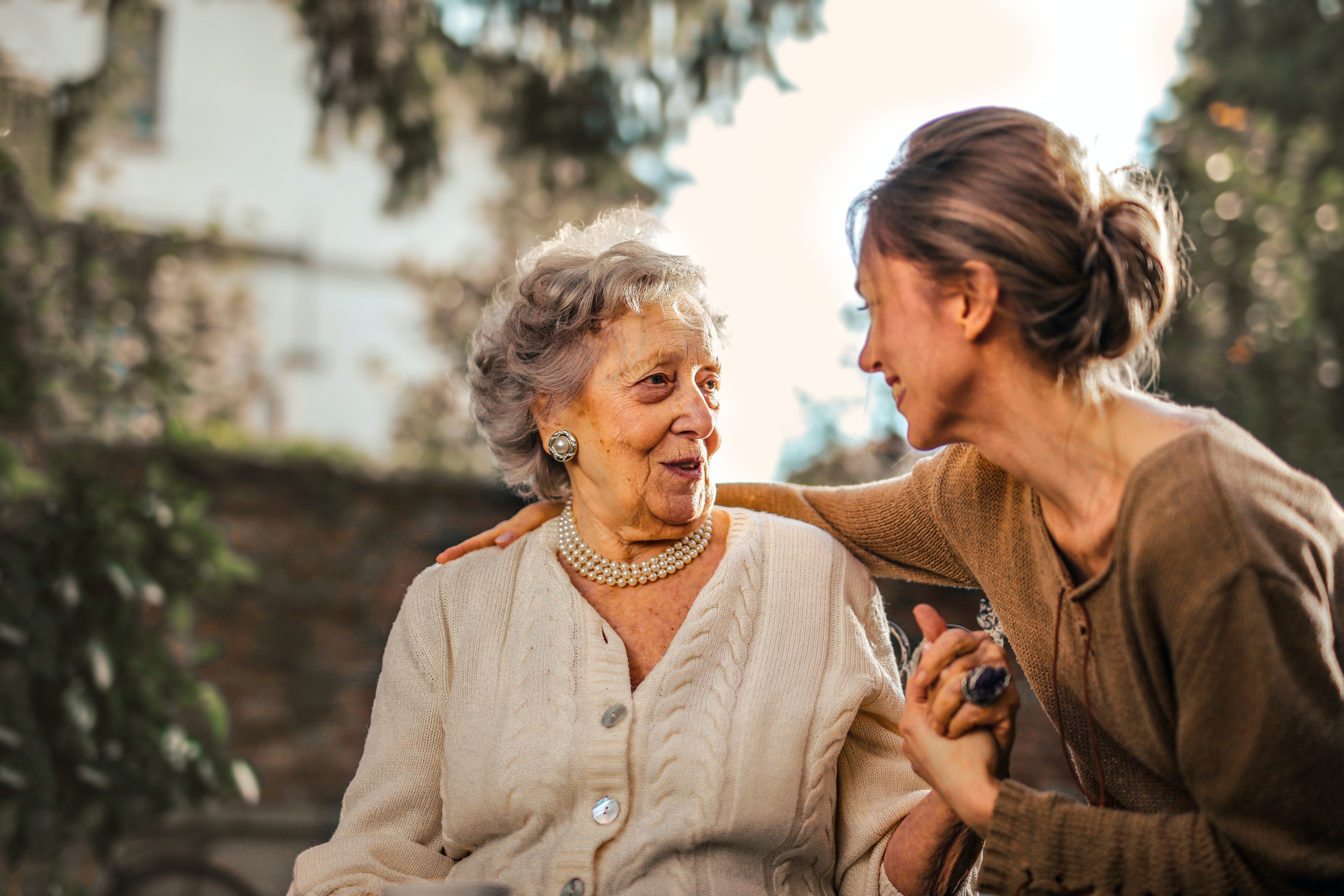 Young woman embracing elderly woman outdoors, both smiling warmly at each other
